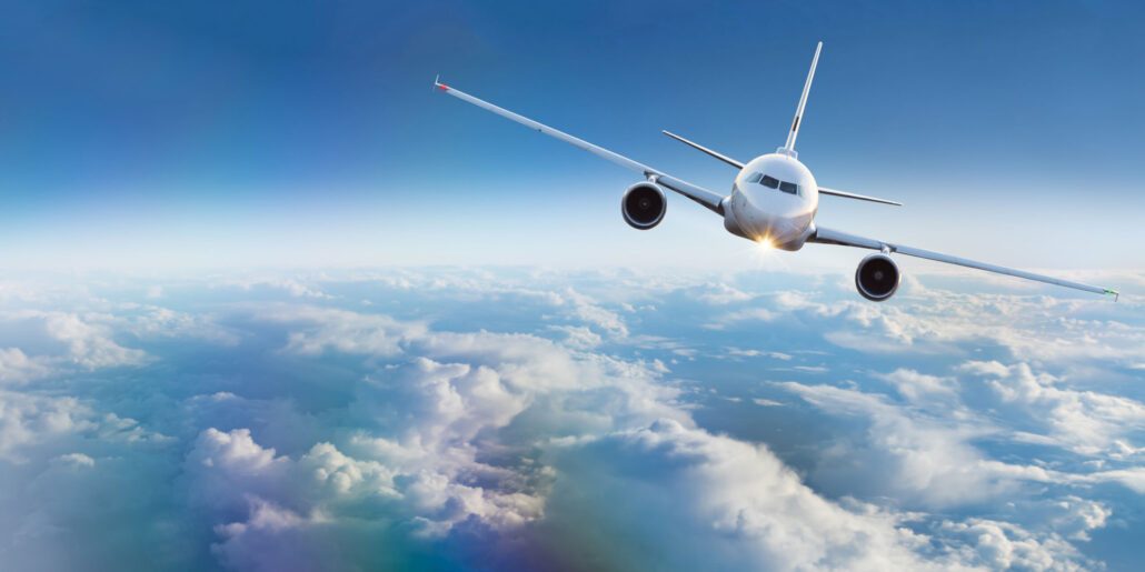 Commercial plane flying on sunny day above clouds